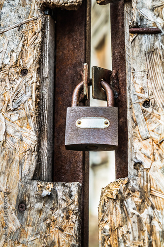 Abandoned building, with a fiberboard gate closed with a padlock in the foreground - focus on the padlock