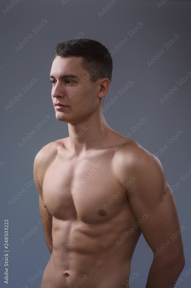 Beautiful young European athletic with bare torso, nice abs and muscles on white and gray background Beautiful young European athletic with bare torso, nice abs and muscles on white and gray background