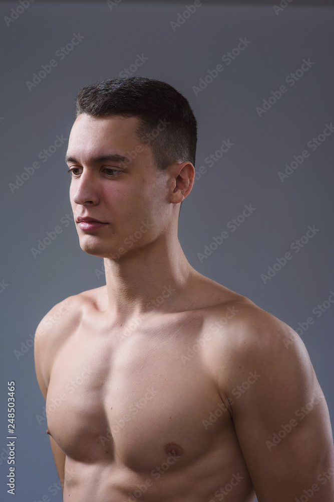 Beautiful young European athletic with bare torso, nice abs and muscles on white and gray background Beautiful young European athletic with bare torso, nice abs and muscles on white and gray background