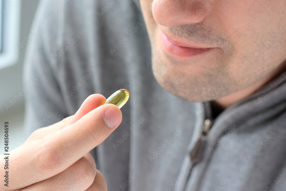 Blurred smiling handsome man in gray sweatshirt on background holding omega  3 soft gel pill in