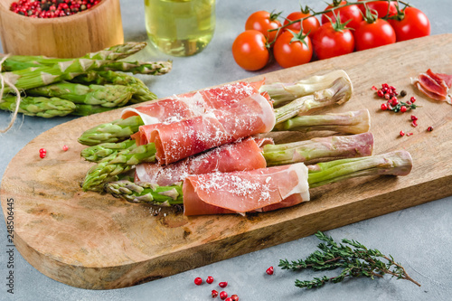 Fresh organic asparagus wrapped in Prosciutto ham on a cutting board.
