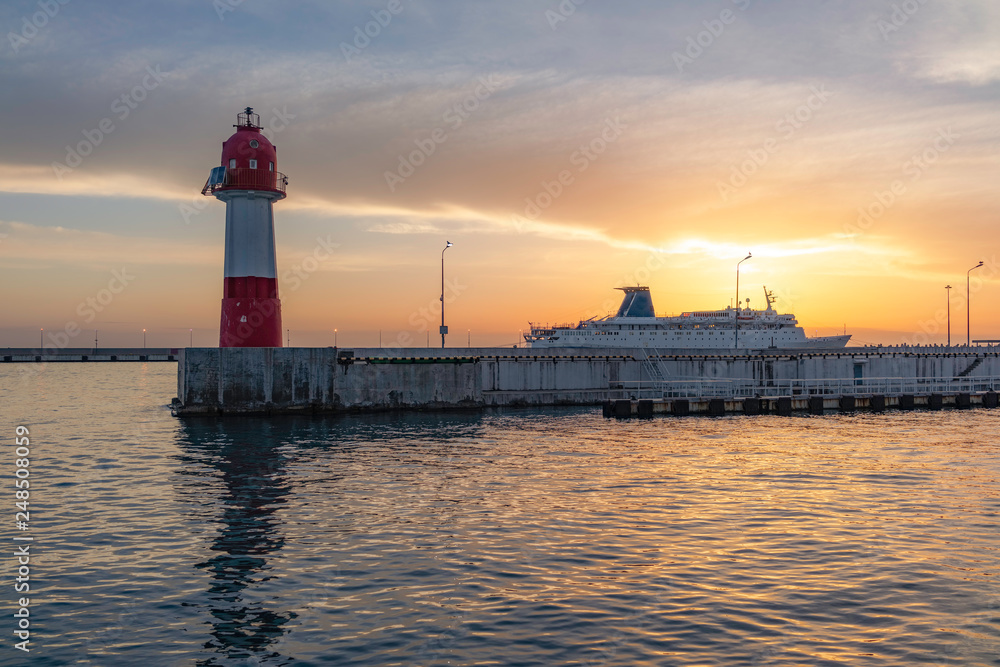 Lighthouse and cruise liner docked in the port, illuminated by the beautiful orange sunset sun