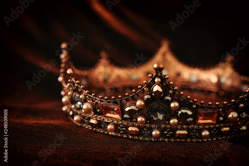 photo of gold crown over gothic dark silk background. Medieval period concept.