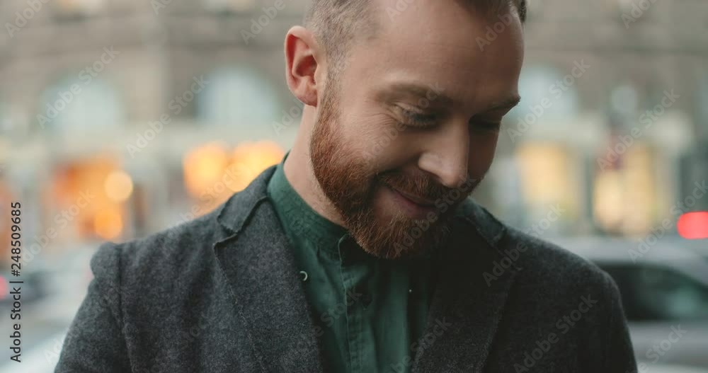 Close up of the smiled young Caucasian man standing outdoors with tablet device in hands, scrooling, tapping and watching something. Portrait. Close up of the smiled young Caucasian man standing outdoors with tablet device in hands, scrooling, tapping and watching something. Portrait.