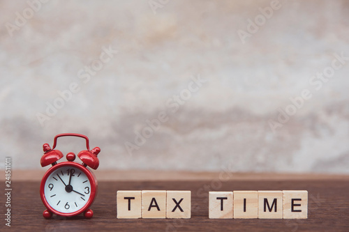 Tax time with Alphabet wooden block cube and Red alarm clock On table dark plank wooden background with copy space