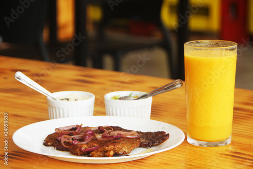 Beef with an orange juice glass on the side, in a restaurant, wooden table