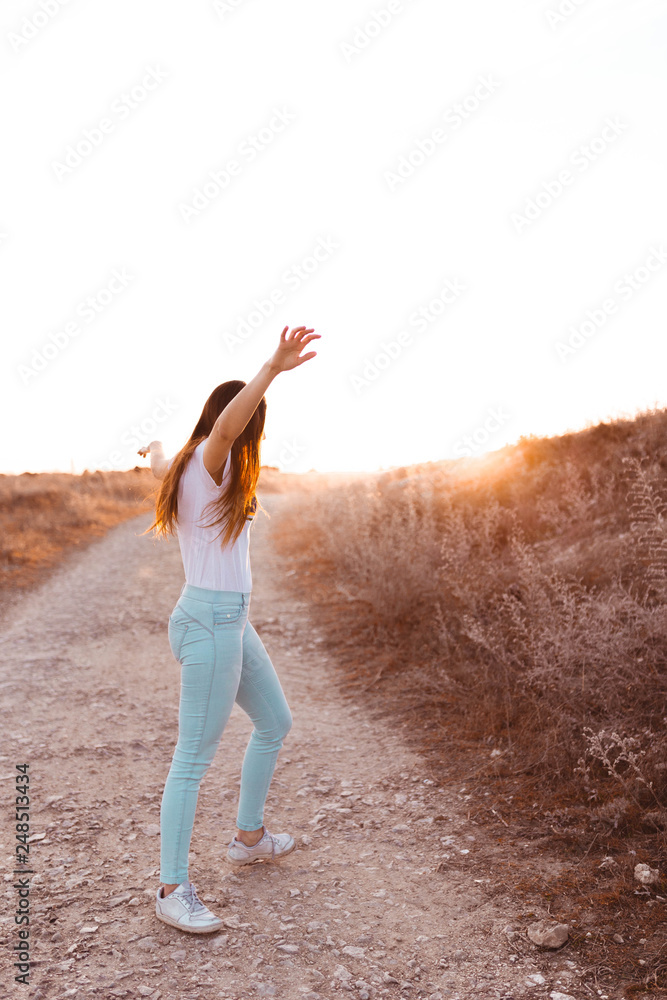 young woman raising arms at sunset in the field young woman raising arms at sunset in the field