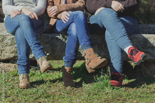 Mujeres sentadas con las piernas cruzadas sobre un banco de piedra con jeans