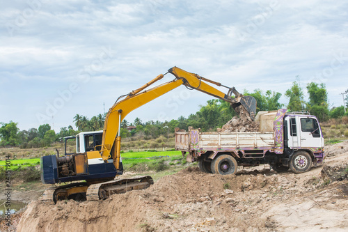 Yellow excavator machine loading soil into a dump truck at construction site