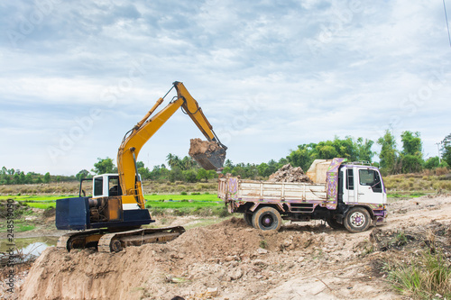 Yellow excavator machine loading soil into a dump truck at construction site