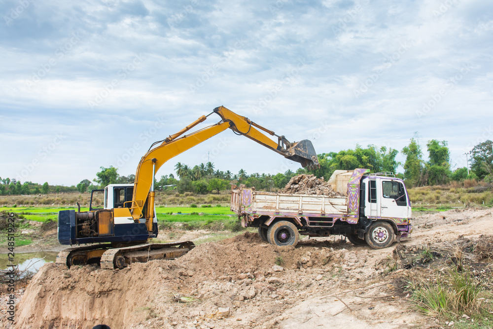 Yellow excavator machine loading soil into a dump truck at construction site Yellow excavator machine loading soil into a dump truck at construction site