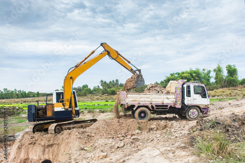 Yellow excavator machine loading soil into a dump truck at construction site