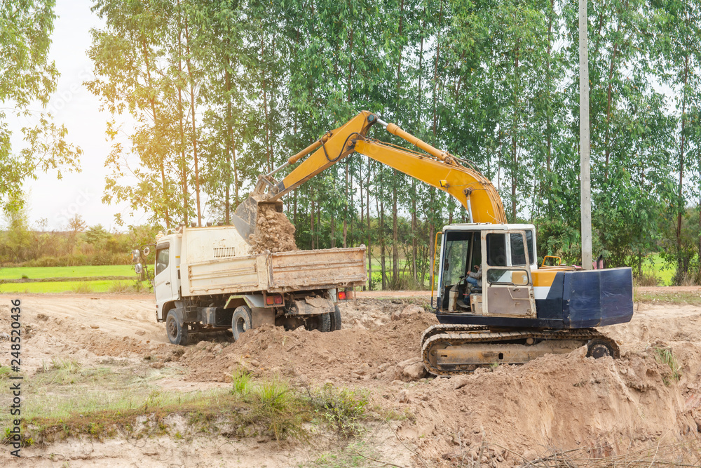 Yellow excavator machine loading soil into a dump truck at construction site