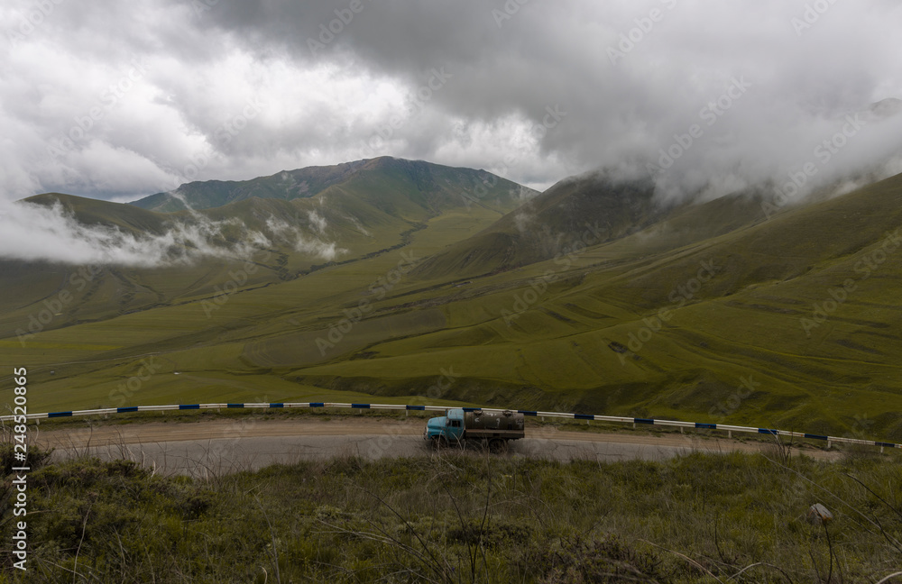 Beautiful landscape, mountain in the clouds. Еhe truck is driving down the road.