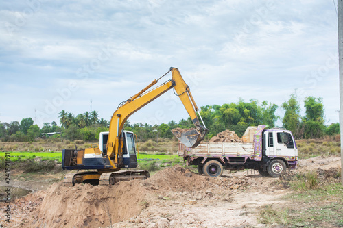 Yellow excavator machine loading soil into a dump truck at construction site
