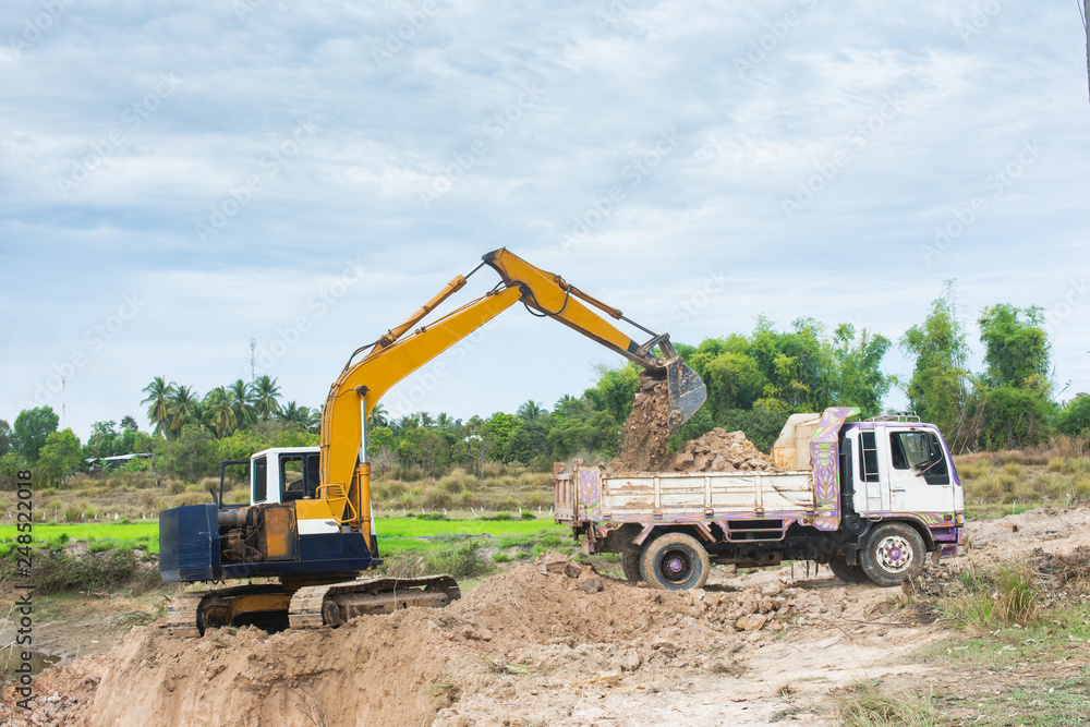 Yellow excavator machine loading soil into a dump truck at construction site