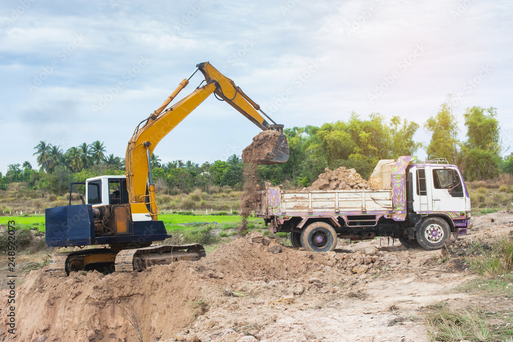 Yellow excavator machine loading soil into a dump truck at construction site Yellow excavator machine loading soil into a dump truck at construction site