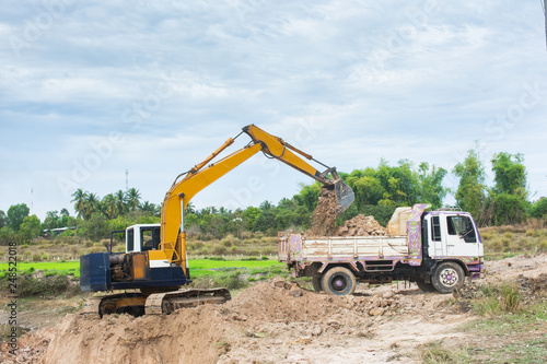 Yellow excavator machine loading soil into a dump truck at construction site