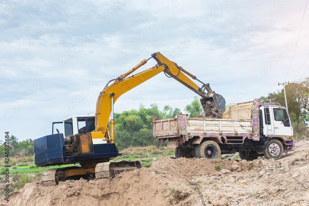 Yellow excavator machine loading soil into a dump truck at construction site Yellow excavator machine loading soil into a dump truck at construction site