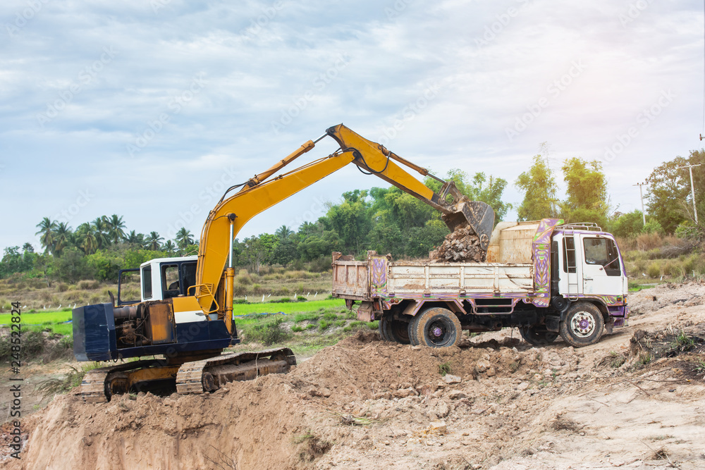 Yellow excavator machine loading soil into a dump truck at construction site Yellow excavator machine loading soil into a dump truck at construction site