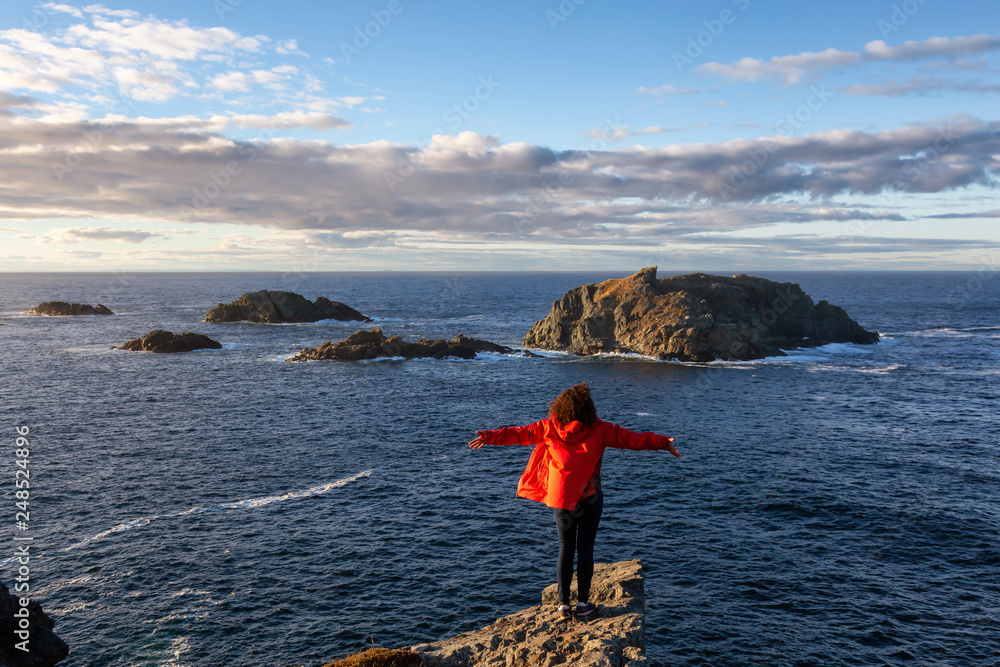 Φωτογραφία Woman in red jacket is standing at the edge of a cliff with open arms and enjoying the beautiful ocean scenery