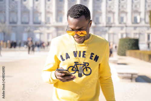 African funny man with sunglasses consults mobile phone in the streets of Madrid Spain.