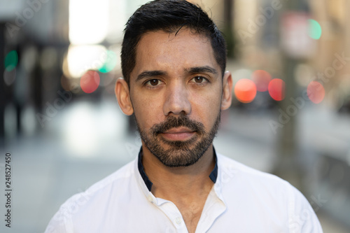 Young Latino Hispanic man in city serious face