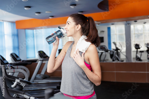Young beautiful woman drinks water on the treadmill in the gym, close-up