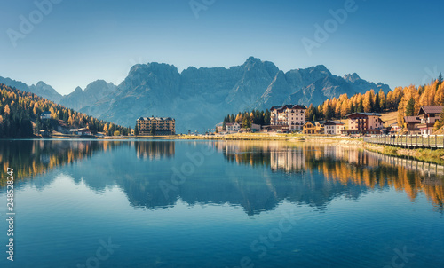 Beautiful famous Misurina lake at sunset in autumn in Dolomites, Italy. Landscape with lake, mountains, blue sky reflected in water, buildings, colorful forest in italian alps. Travel and nature