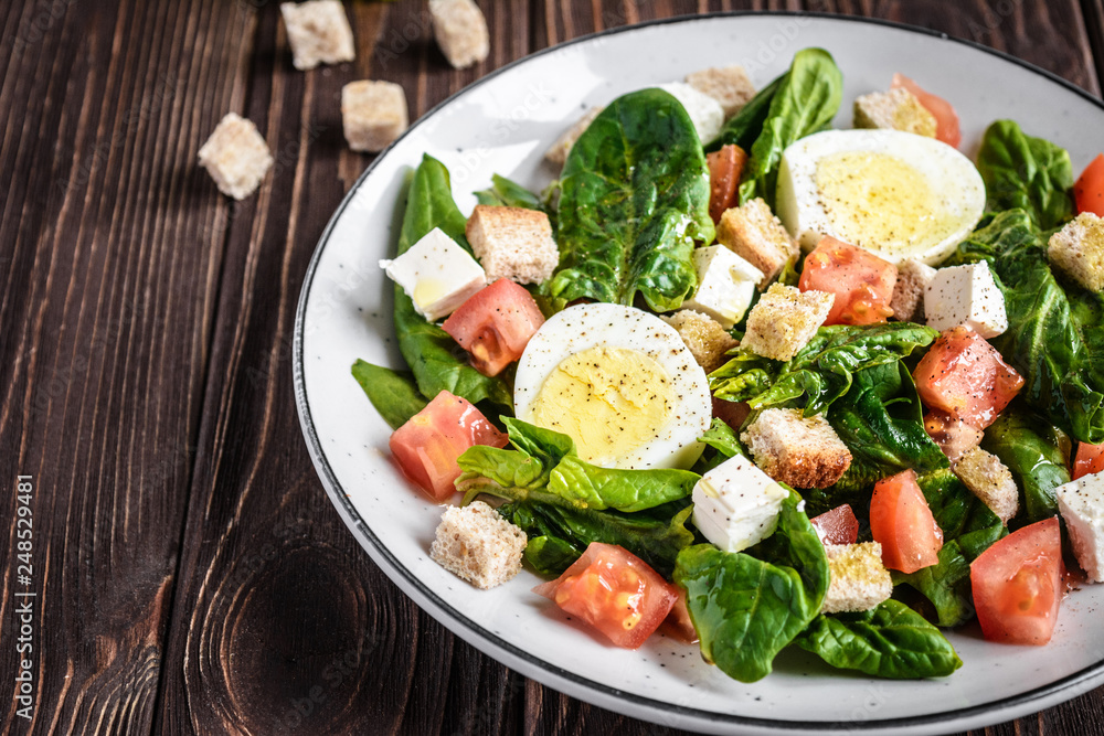 Fresh vegetable salad with tomatoes, spinach, bread crumbs, egg and feta. Healthy food. Dietary dinner or lunch menu. Salad plate on the table.