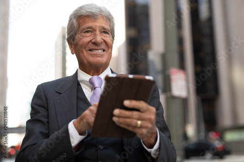 Senior businessman in city walking using tablet computer
