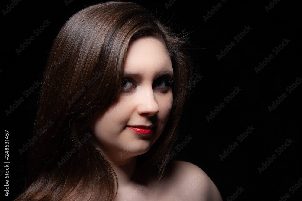 Beautiful gray-eyed brown-haired woman with red lips and bared shoulders against black background. Closeup studio portrait Beautiful gray-eyed brown-haired woman with red lips and bared shoulders against black background. Closeup studio portrait