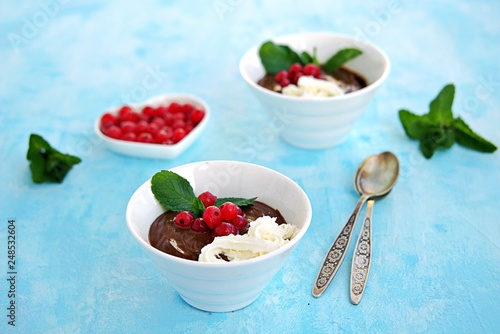 Sweet dessert, chocolate pudding in white portioned saucers on a light blue background. Served with whipped cream and red currant berries. Valentine's Day concept.