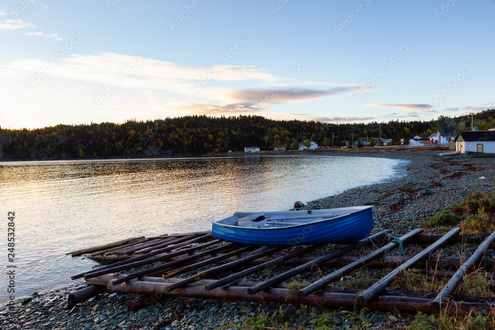Wooden boat laying by the Atlantic Ocean Shore during a vibrant sunrise. Taken in Beachside, Newfoundland, Canada.
