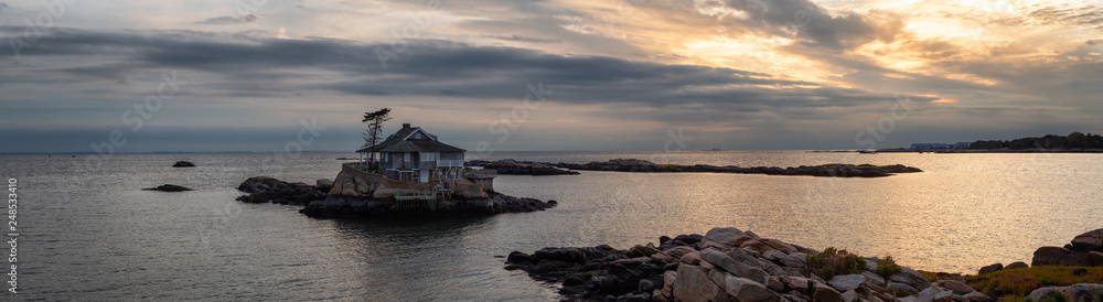 Panoramic seascape view of a beautiful home on a rocky island during a vibrant sunset. Taken on the Atlantic Ocean in New Haven, Connecticut, United States. Panoramic seascape view of a beautiful home on a rocky island during a vibrant sunset. Taken on the Atlantic Ocean in New Haven, Connecticut, United States.