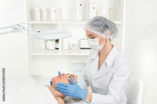 Female beautician doctor with patient in wellness center. Professional cosmetologist make procedure to beautiful girl in cosmetology cabinet or beauty parlor.