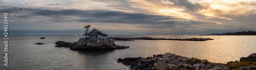 Panoramic seascape view of a beautiful home on a rocky island during a vibrant sunset. Taken on the Atlantic Ocean in New Haven  Connecticut  United States.