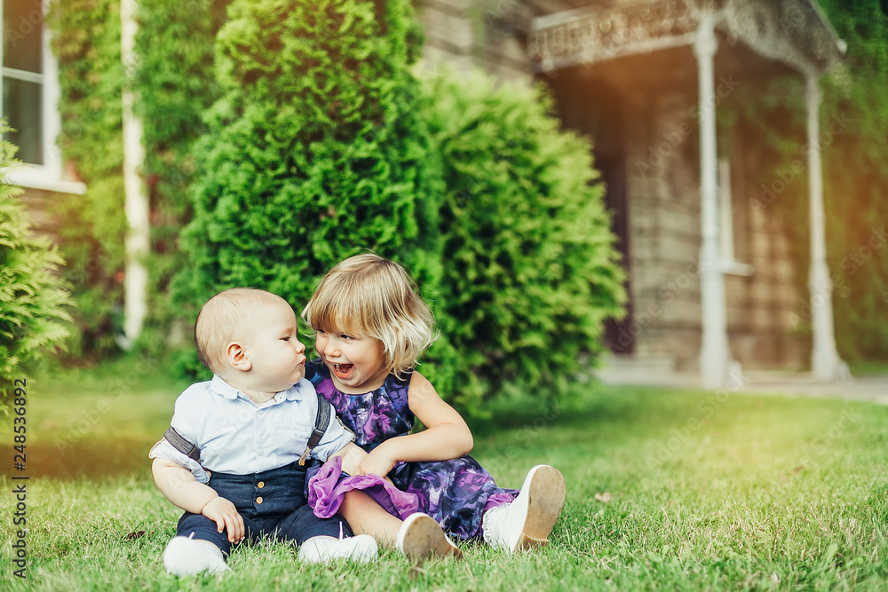 Summer happy time. Two cheerful infant babies outdoors smiling and playing together in green sunny park. Childhood, happiness, infant baby concept Summer happy time. Two cheerful infant babies outdoors smiling and playing together in green sunny park. Childhood, happiness, infant baby concept