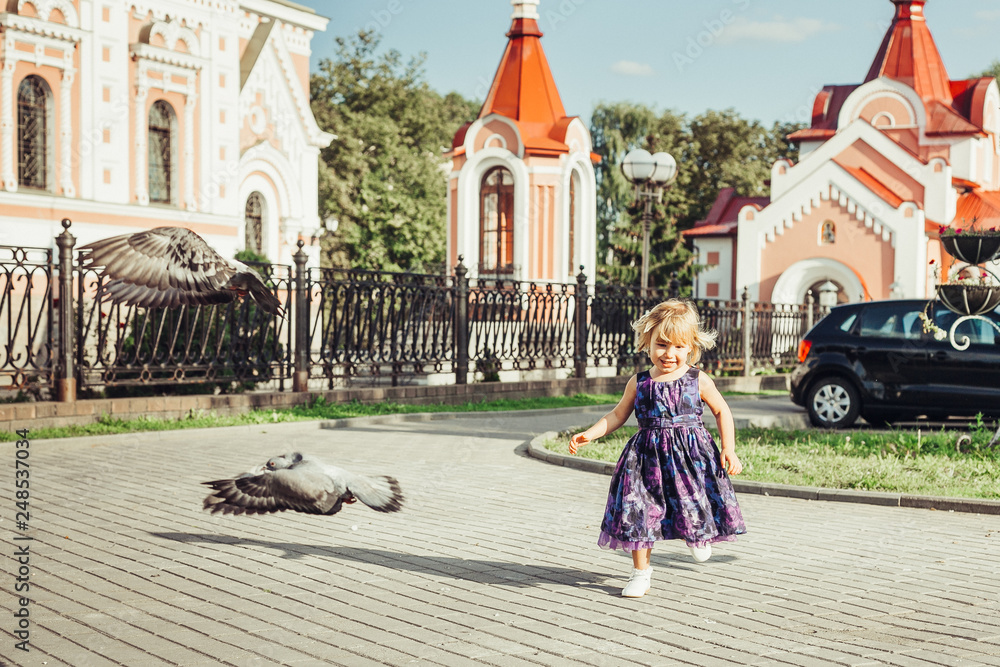 Little cute girl running outdoors with pigeons