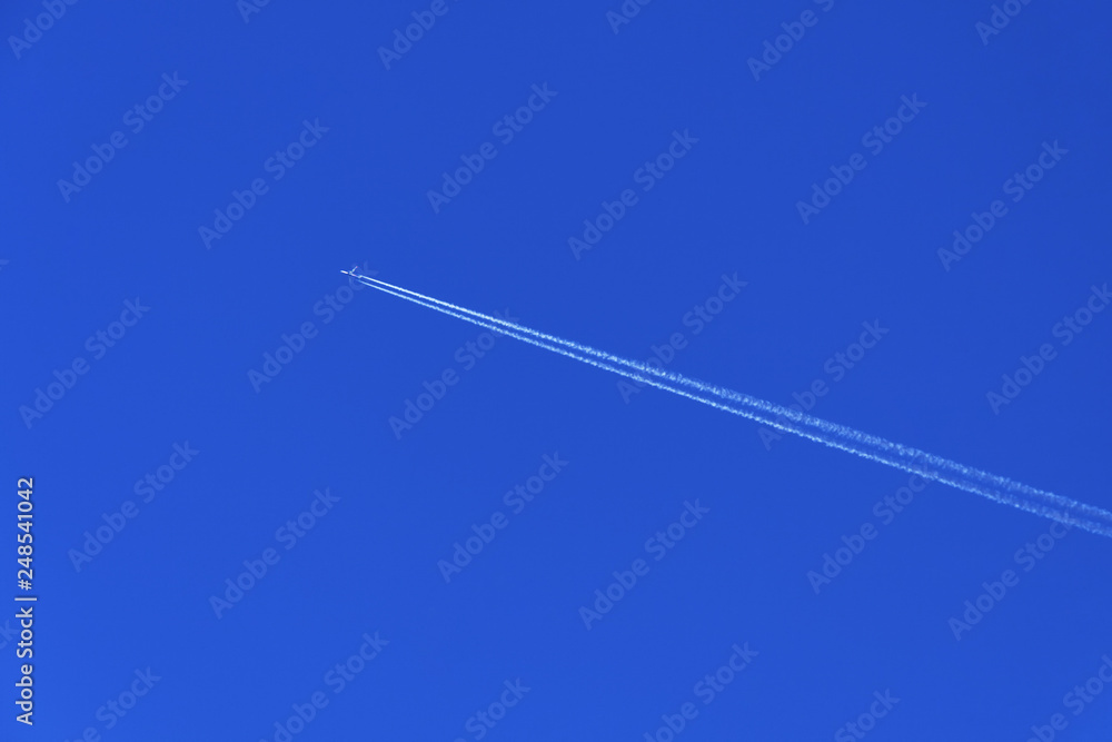 Flight of the plane with a white trace diagonally against a clear blue sky Flight of the plane with a white trace diagonally against a clear blue sky
