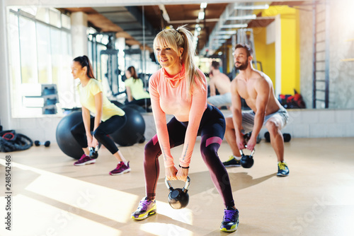 Small group of people with healthy habits swinging kettlebell. Gym interior  mirror in background.male