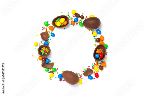 Broken and whole chocolate eggs, multi-colored sweets on a white background. Happy Easter. Circle shape. Concept of celebrating Easter, Easter decorations. Flat lay, top view. Copy space