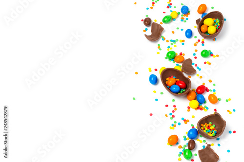 Broken and whole chocolate Easter eggs, multicolored sweets on white background. Concept of celebrating Easter, Easter decorations, search for sweets for Easter Bunny. Flat lay, top view. Copy Space