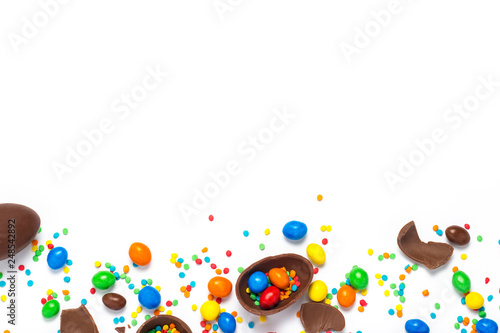 Broken and whole chocolate Easter eggs, multicolored sweets on white background. Concept of celebrating Easter, Easter decorations, search for sweets for Easter Bunny. Flat lay, top view. Copy Space