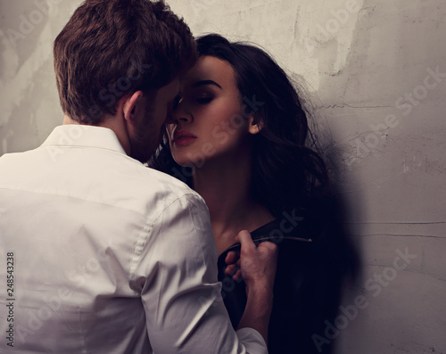 Sexy couple portrait. Man in white shirt kissing his sensual beautiful girlfriend with much emotion in dark drama light with dark shadow. Closeup
