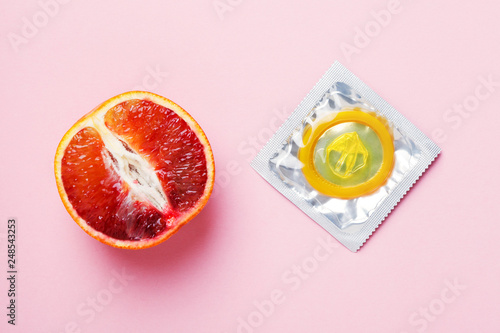 fresh grapefruit and yellow condom on pink background