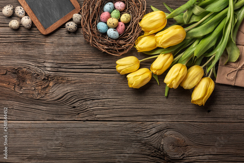 Yellow tulips in a paper bag, a nest with Easter eggs on a wooden background. Top view with copy space.