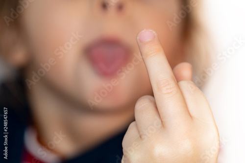 Small naughty child on white background is showing middle finger and tongue, impolite and rude fuck off expression photo