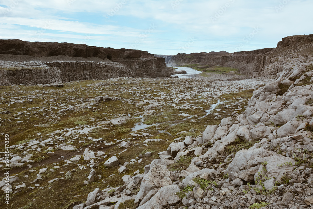 View to river of Dettifoss waterfall and mountains, rocks in the foreground, river is in perspective, film look, Iceland, summer