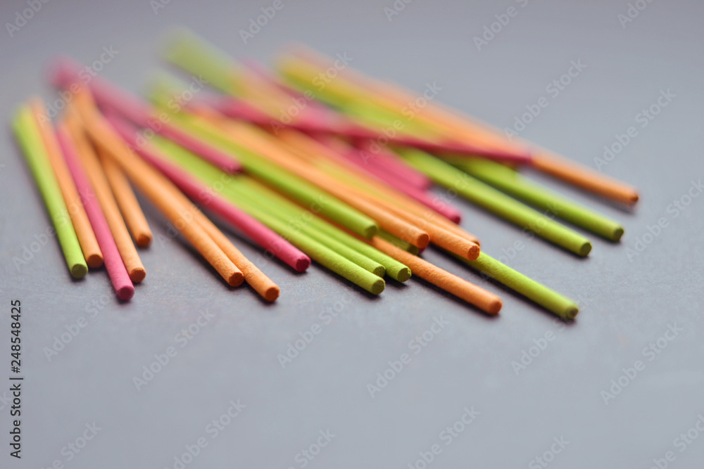 Multi-colored short Indian incense sticks lie on a dark gray background closeup, with copyspace